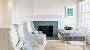 A room with a fireplace, a dining table with a plant, and two upholstered chairs. - 8BR Pondfront Estate with Ocean Views, Pool, Spa, Tennis and Golf Club Access (Nantucket)
