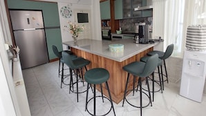 A kitchen with a central island, bar stools, a refrigerator, a coffee maker, and a water dispenser. - Tranquil 3-bedroom House in Eğirdir With Stunning Views (Egirdir)