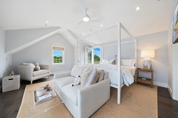 A modern bedroom with a sloped ceiling, a large window, a bed with a canopy, and a bedside table with a lamp.