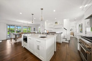 A modern kitchen with a large island, white cabinetry, and a stainless steel range hood.