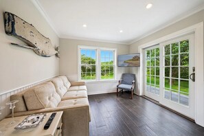 A room with a beige sofa, a chair, and a television on the wall.