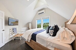 A bedroom with a bed, a chair, a window, and an air conditioning unit.