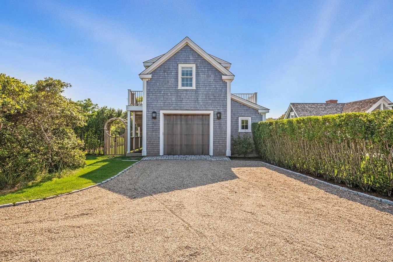 A two-story house with a front garage, a gravel driveway, and a well-maintained hedge.