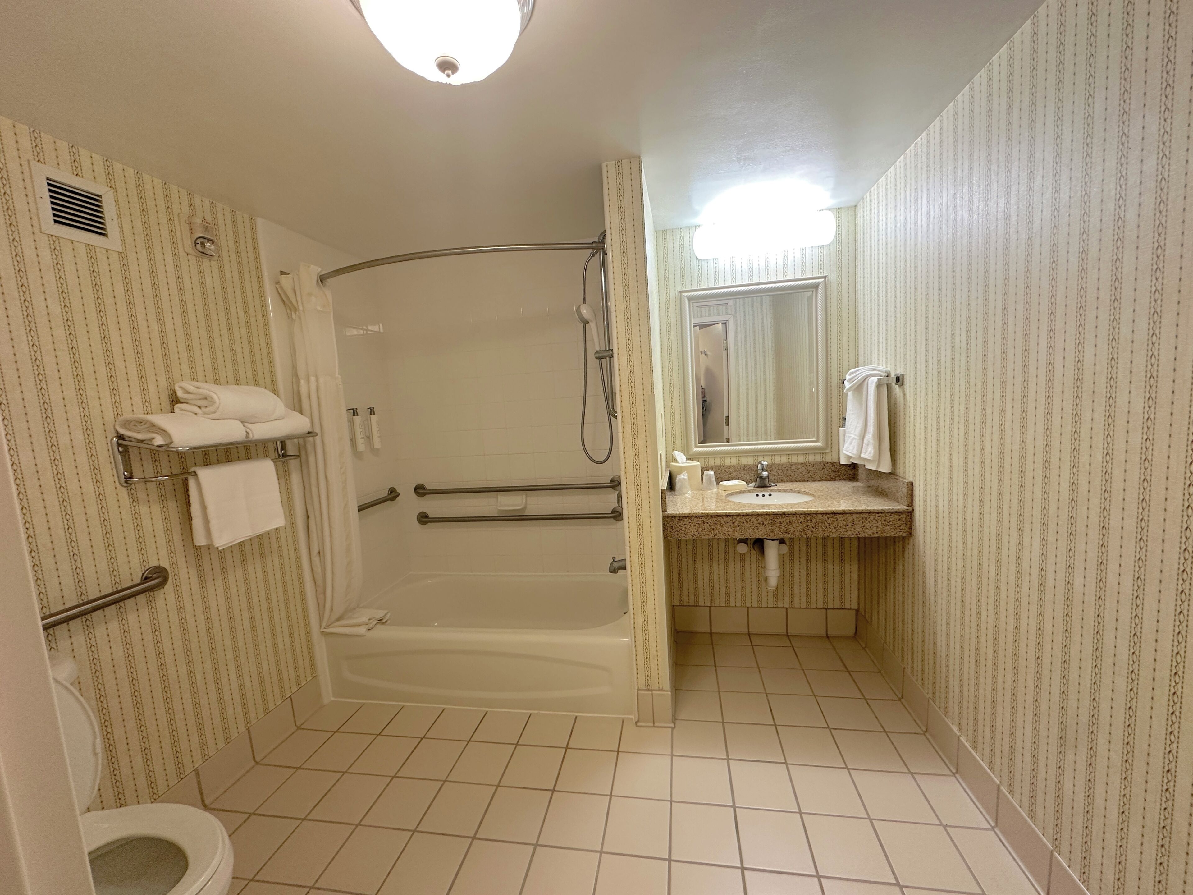 A bathroom with a shower, toilet, and sink, featuring patterned wallpaper and a tiled floor.