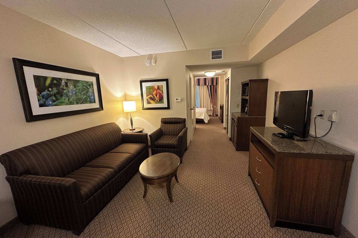 A hotel room with a sofa, armchair, small table, TV, and a cabinet.