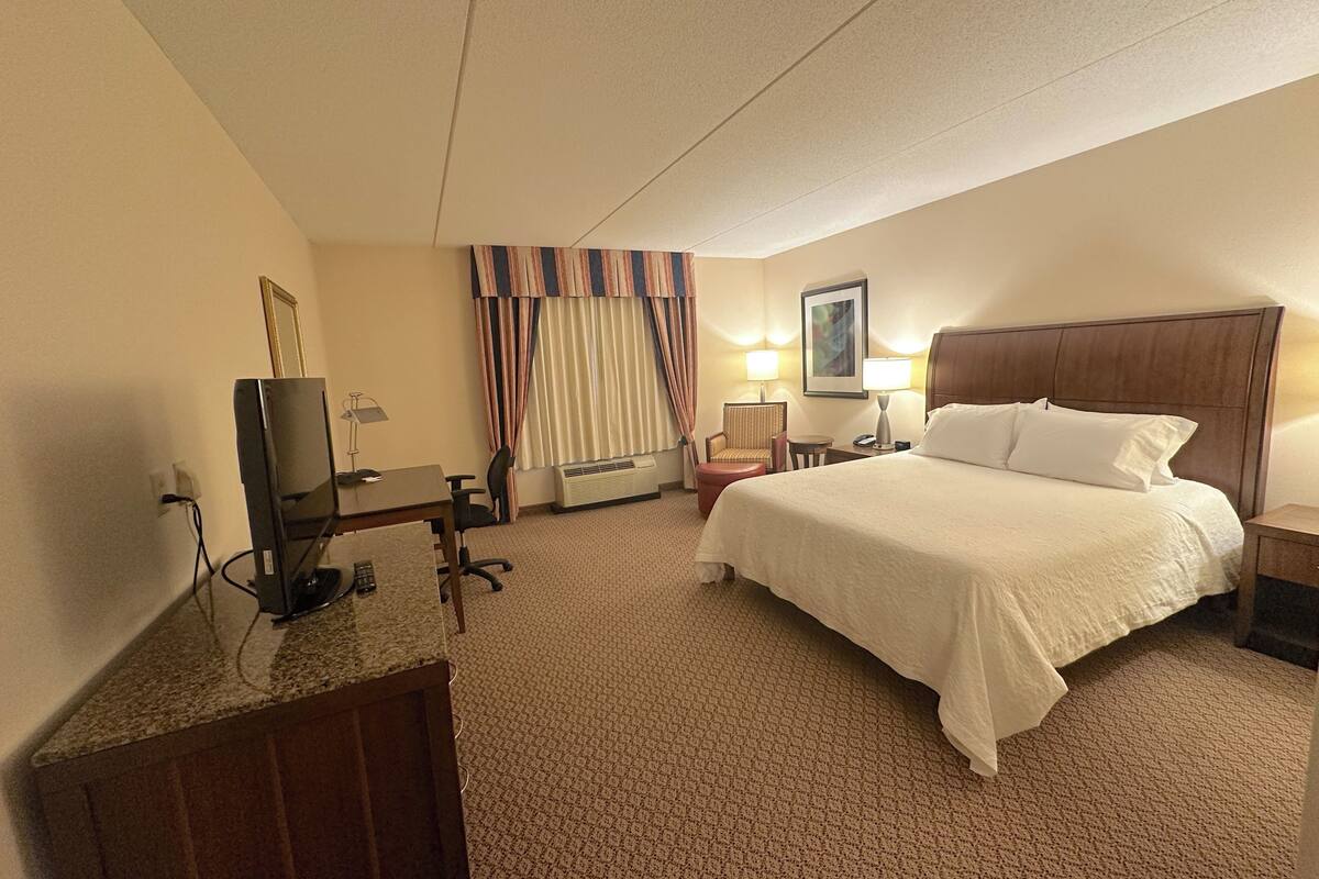 A hotel room with a bed, desk, television, and a window with curtains.