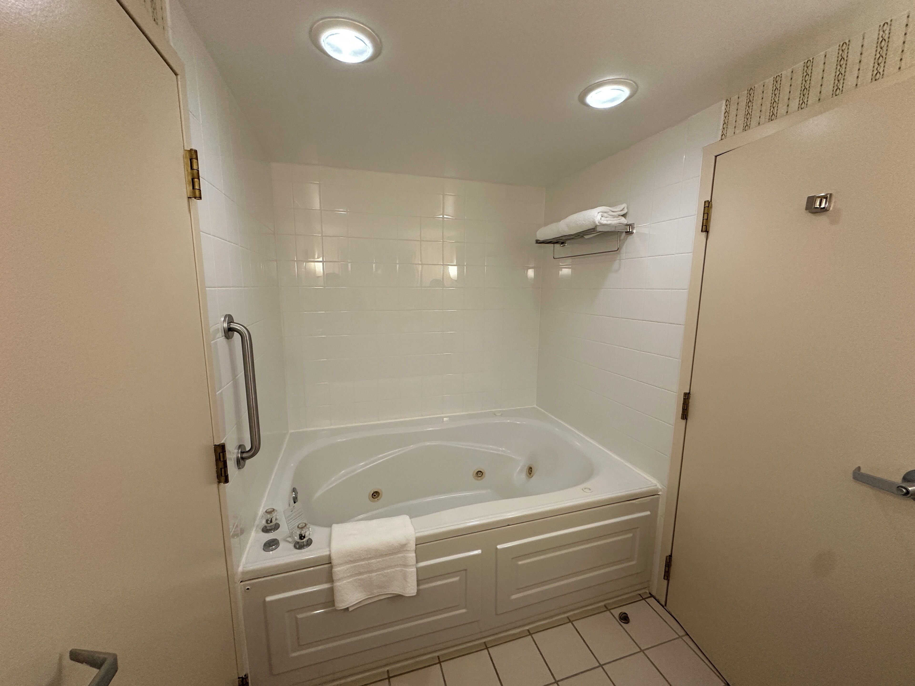 A bathroom with a bathtub, a handrail, a towel rack, and a toilet.