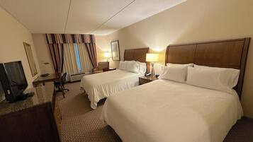 A hotel room with two beds, a desk, a television, and a window with curtains.