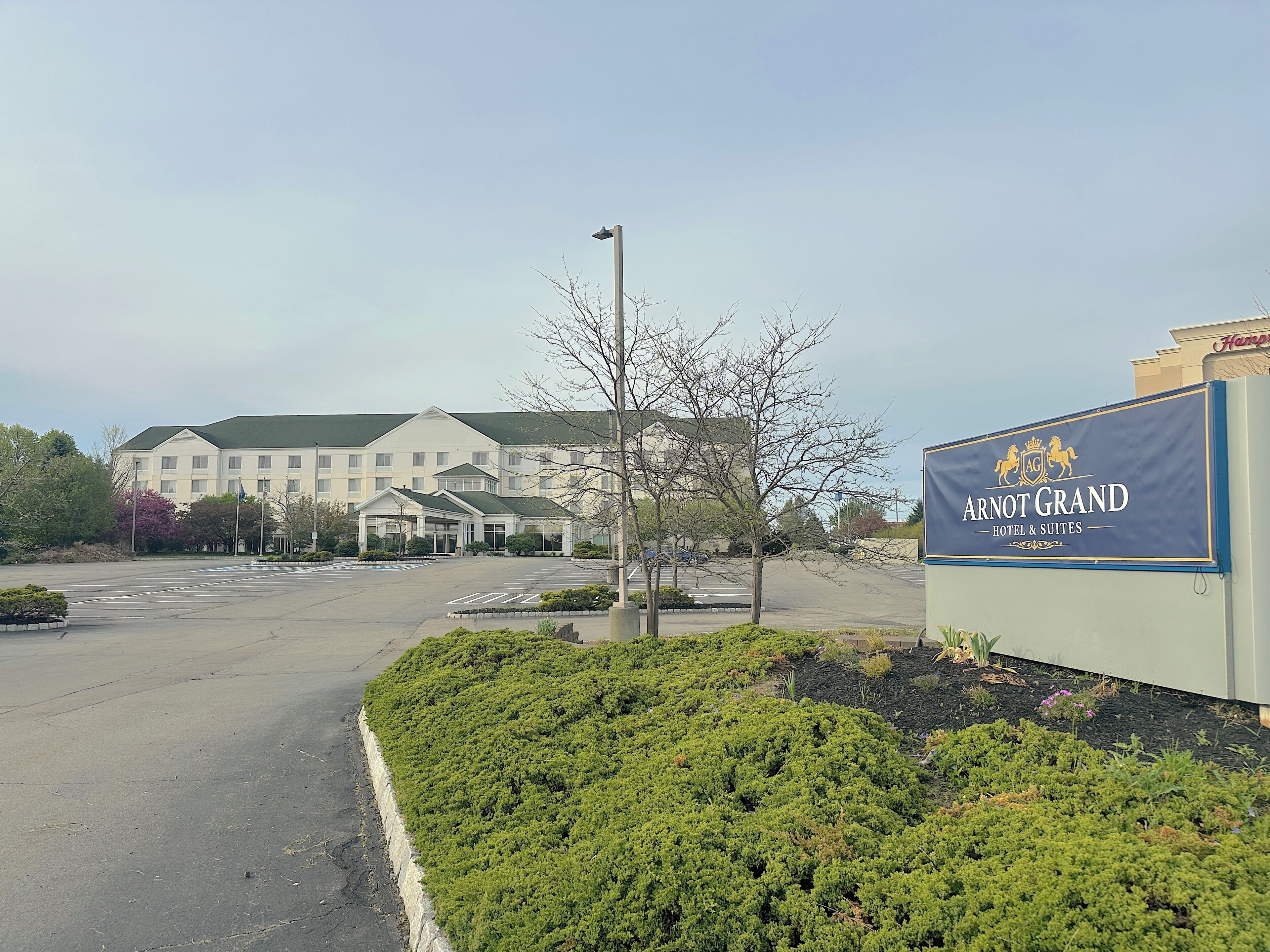 Een hotel ingang met een bord voor Arnot Grand Hotel & Suites, een parkeerplaats en een aangelegde zone met struiken.