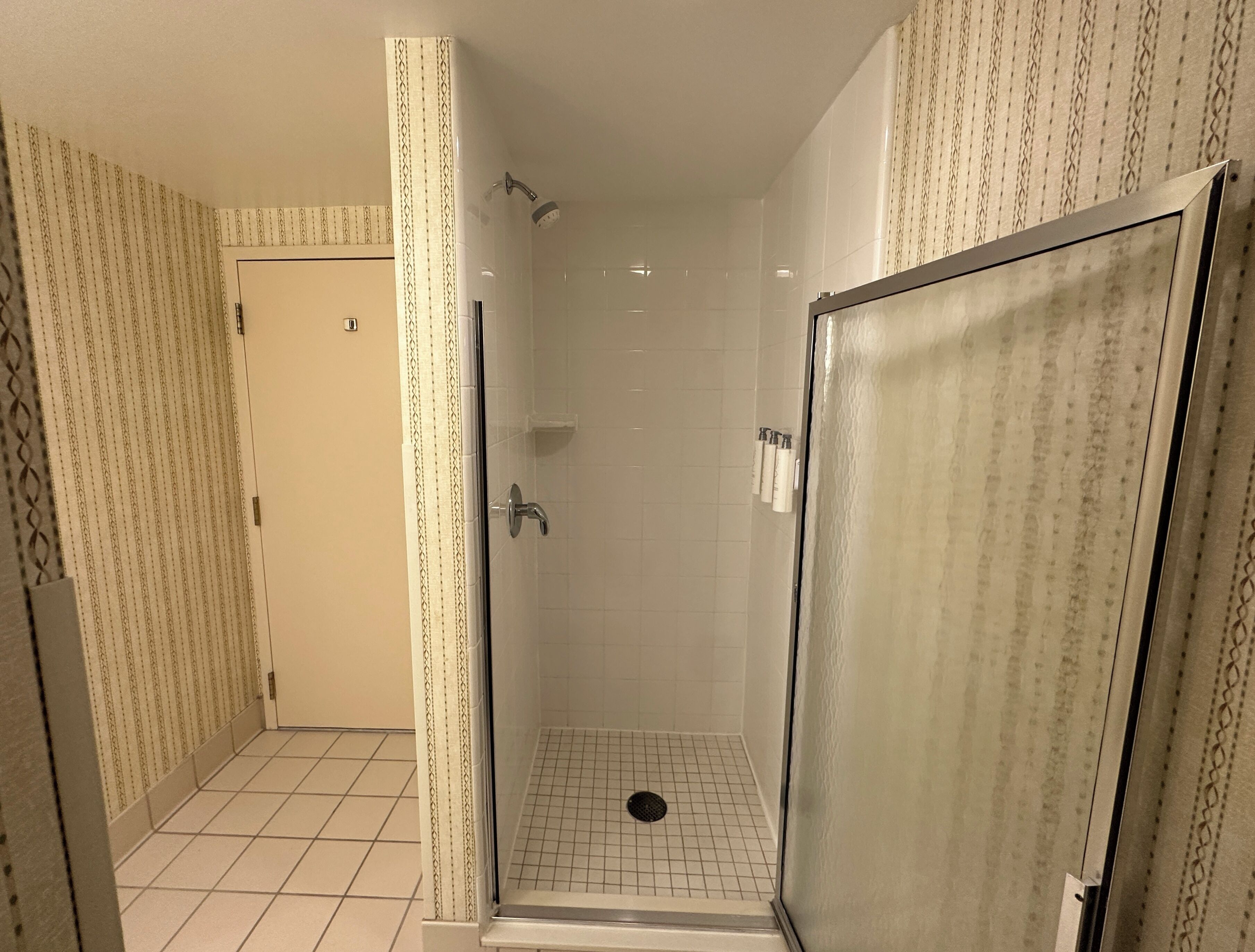A bathroom with a glass-enclosed shower, tiled floor, and patterned wallpaper.
