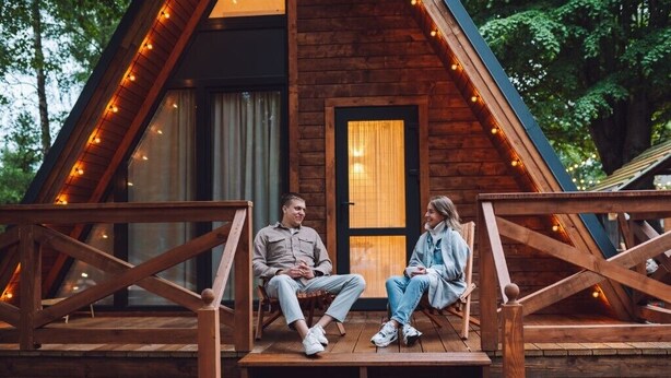 A wooden cabin with a porch, two people sitting, and string lights. - Hotel Regency Inn Dhirkot (Rawalakot)
