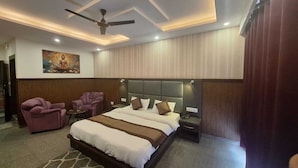 A modern hotel room with a large bed, a ceiling fan, a painting, and a seating area with chairs. - Hotel Summer Nest - Bhagsu Waterfall  (Dharamshala)