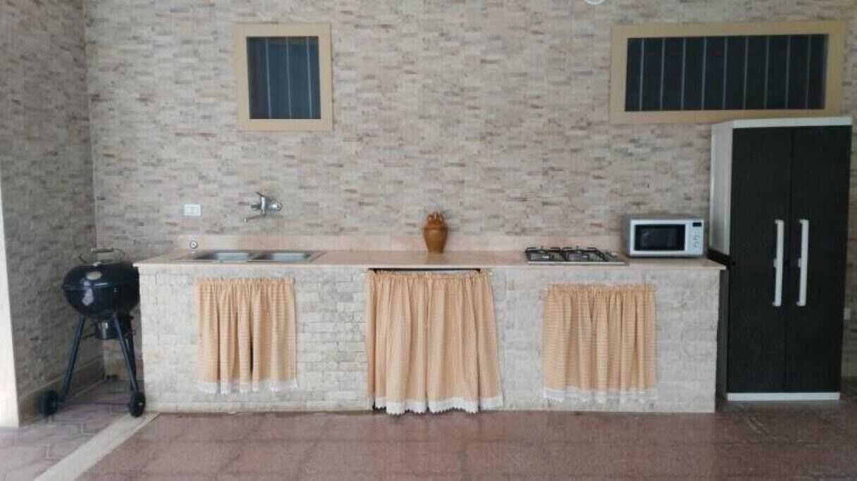 Una cucina con lavello, fornelli e forno a microonde, un frigorifero nero e un piccolo finestrino.