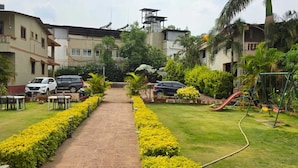 A residential area with a paved pathway, parked cars, a playground, and a building with a balcony. - Prince Palace Bhilar in Village of Books (Bhilar)