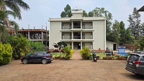 A multi-story building with a central entrance, surrounded by greenery and parked vehicles. - Prince Palace Bhilar in Village of Books (Bhilar)