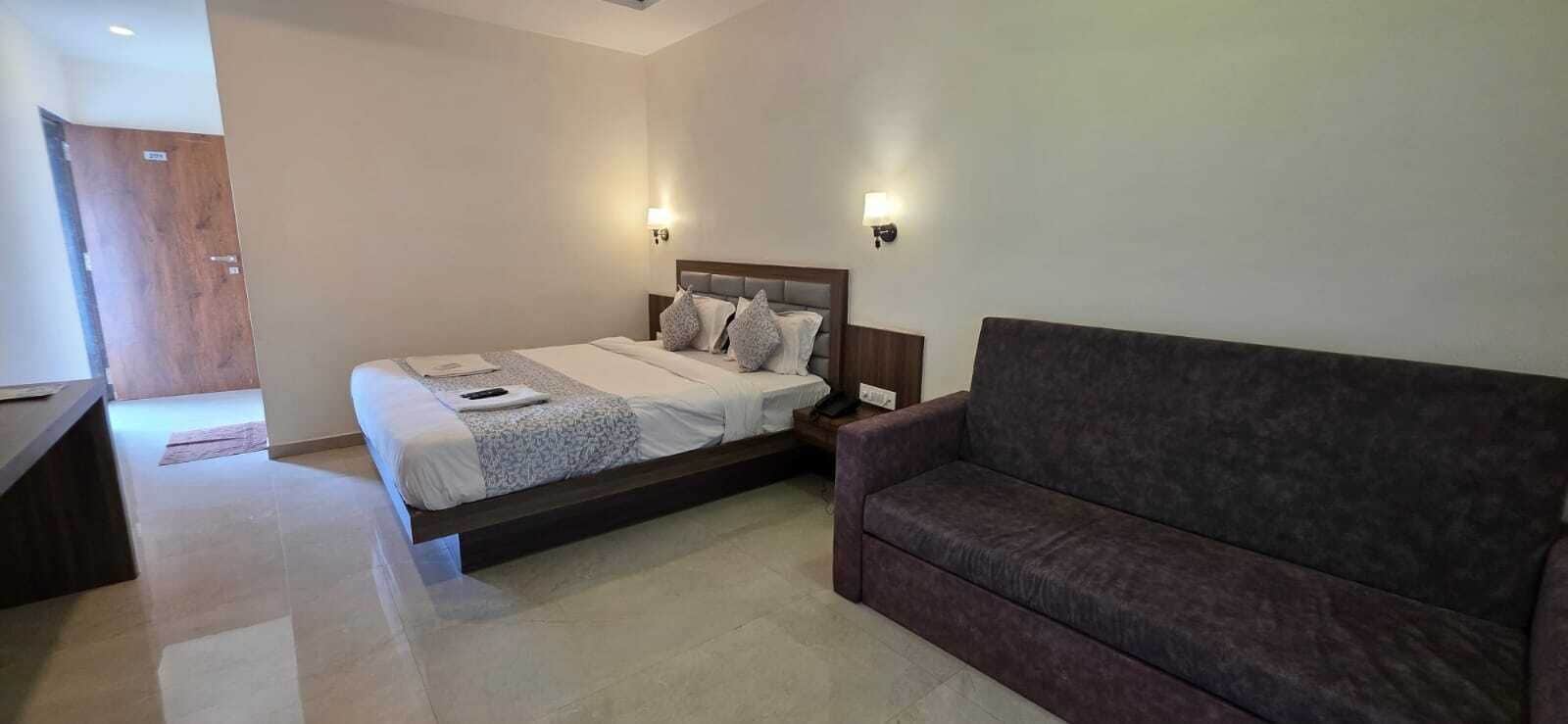 A bedroom with a bed, a nightstand, a wooden door, and a brown sofa.