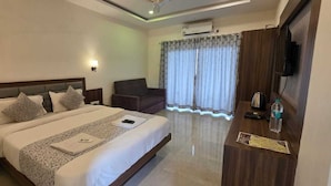 A hotel room with a bed, a desk, a chair, a TV, and a window with curtains. - Prince Palace Bhilar in Village of Books (Bhilar)