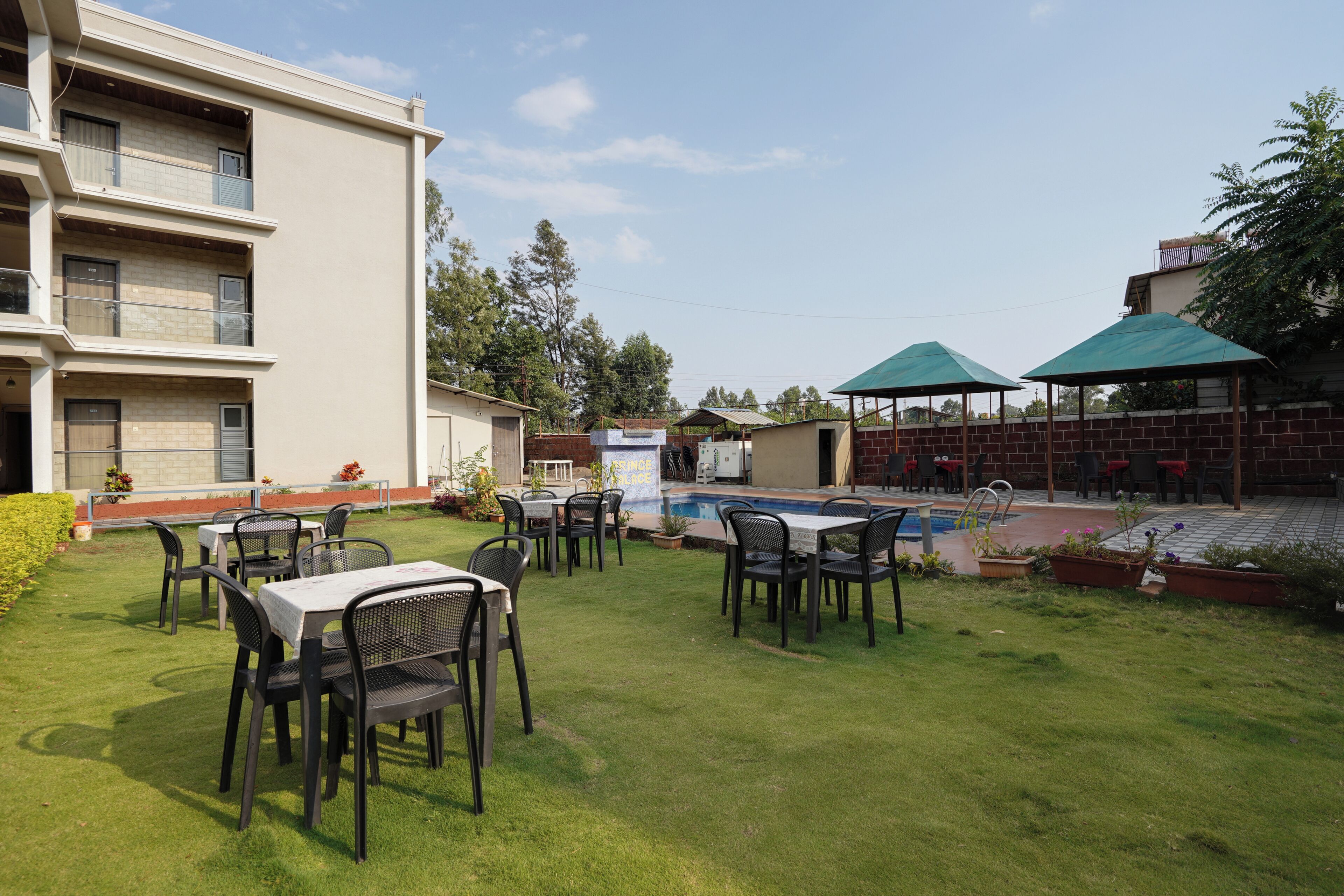 Un patio de hotel con mobiliario exterior, piscina y un edificio de varios pisos.
