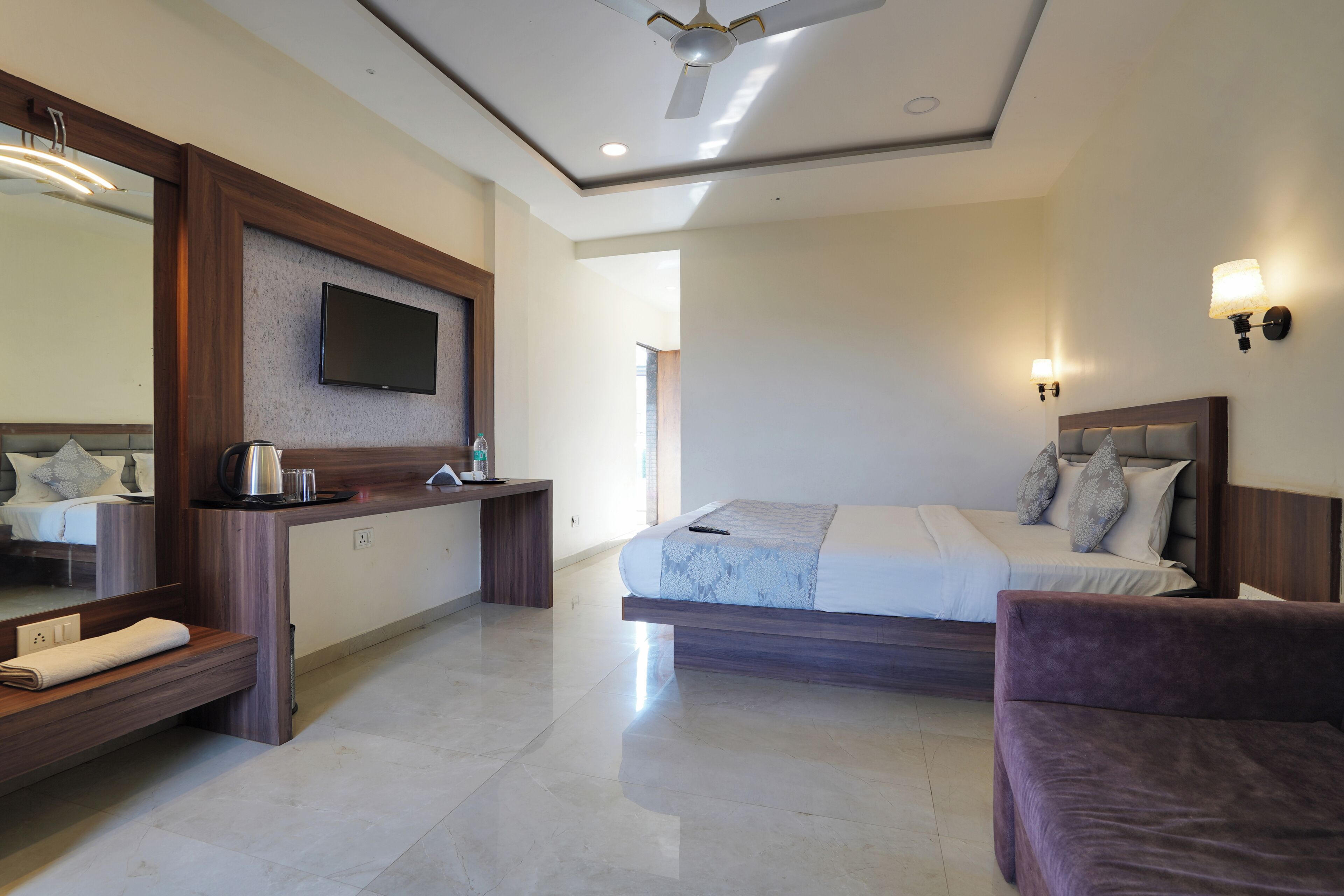 A hotel room with a bed, a desk, a chair, a television, and a ceiling fan.