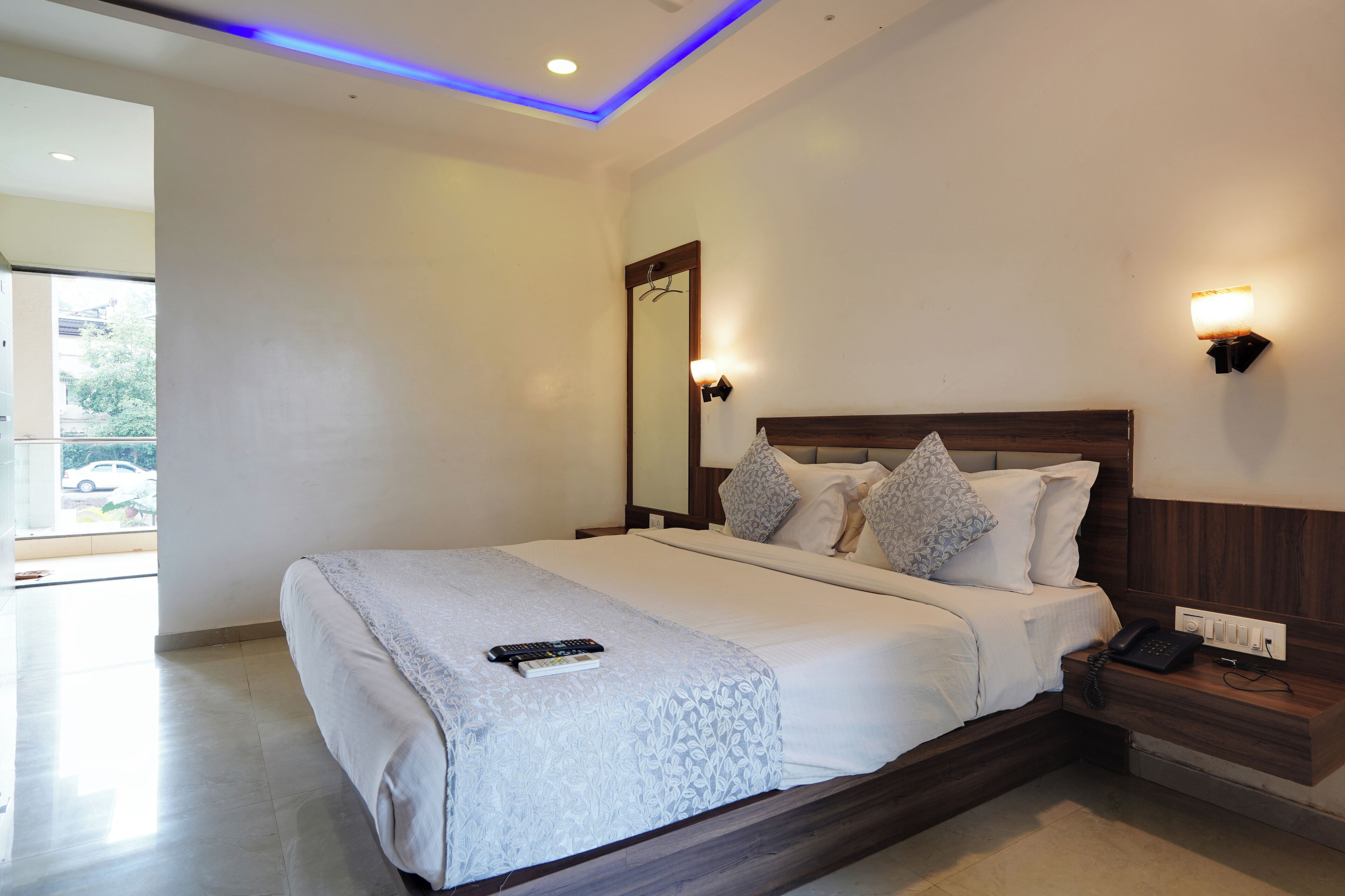 A hotel room with a large bed, a bedside table, a mirror, and a wall-mounted light fixture.