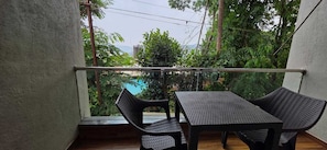 A balcony with a table and chairs, overlooking a lush garden and a distant building. - Prince Palace Bhilar in Village of Books (Bhilar)