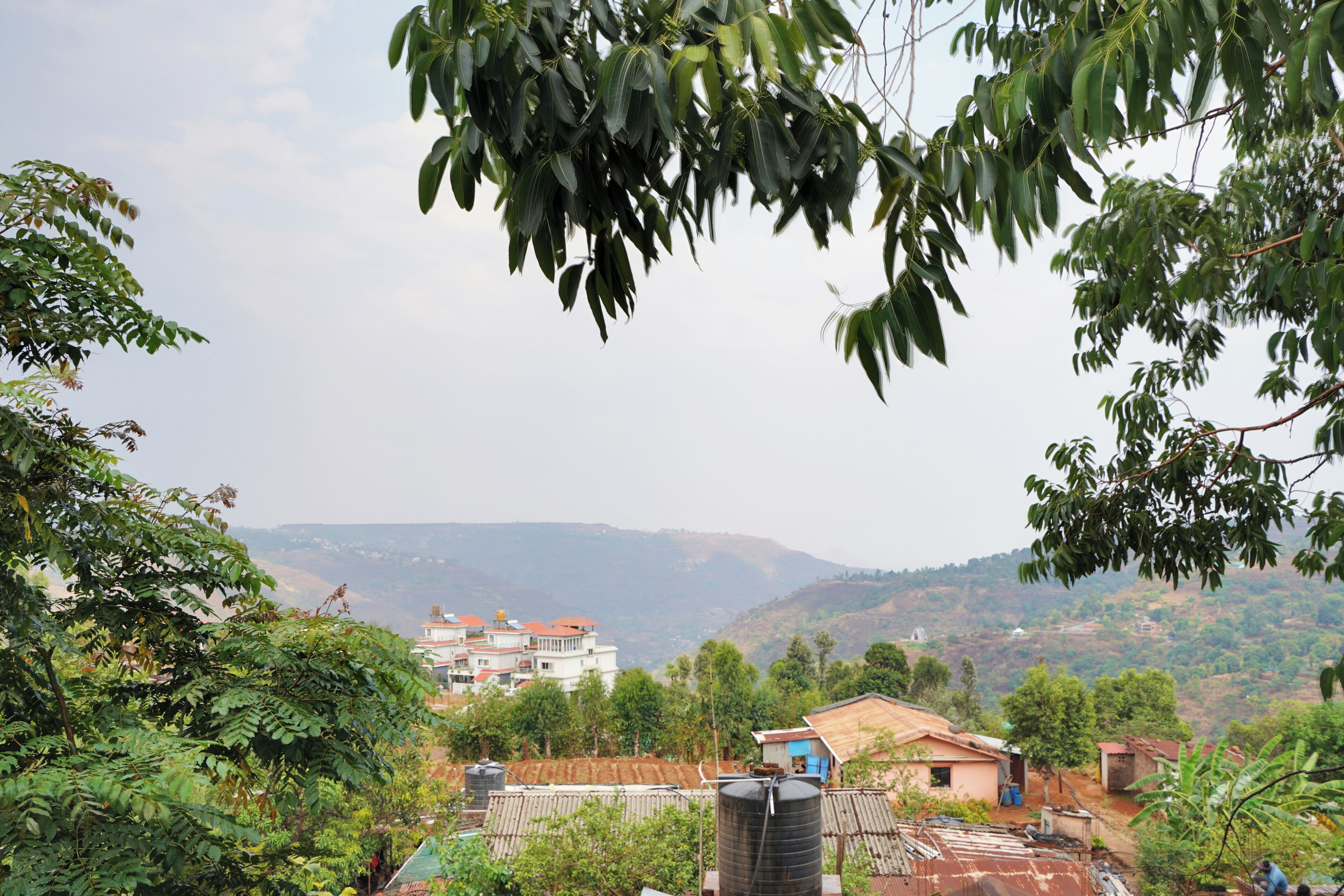 A residential area with houses, a water tank, and a hilly landscape in the background.