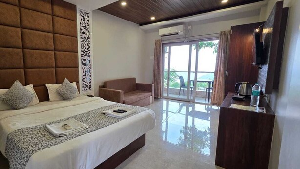 A hotel room with a large bed, a sofa, a desk with a kettle, and a view of the outdoors. - Prince Palace Bhilar in Village of Books (Bhilar)