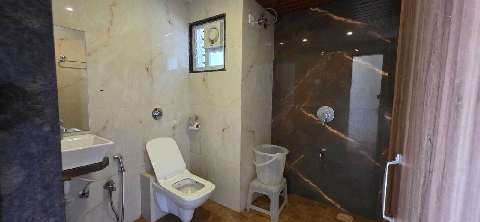 Et badeværelse med toilet, håndvask, brusebad og en marmorvæg.