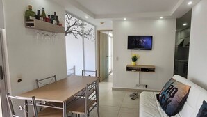 En moderne stue med spiseområde, et fjernsyn ophængt på væggen og en sofa med pude.