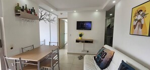 Ein modernes Wohnzimmer mit Essbereich, einem an der Wand montierten Fernseher und einer Couch mit Kissen.