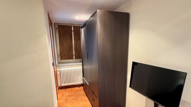 Et soveværelse med seng, fjernsyn, garderobeskab og en radiator.