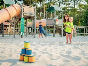 A playground with slides and climbing structures, a sandpit with stacked toys, and a wooden fence. - COZY HOUSE - LODGING 8p LUXURY CAMPING RANGE **** (Lège-Cap-Ferret)