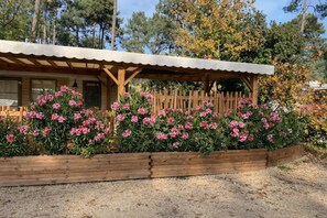 Une cabane en bois dotée d’un porche couvert, entourée d’un jardin où poussent des fleurs roses.