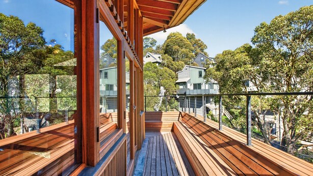 Una terrazza in legno con ringhiera in vetro, affacciata su una zona residenziale con case e alberi.