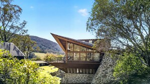 Una casa moderna con facciata in pietra, un pontile in legno e vista su un paesaggio collinare.