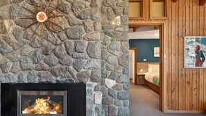 A stone wall with a fireplace and a wooden door leading to a bedroom. - Wombiana: Iconic Design in the Heart of Thredbo (Thredbo)