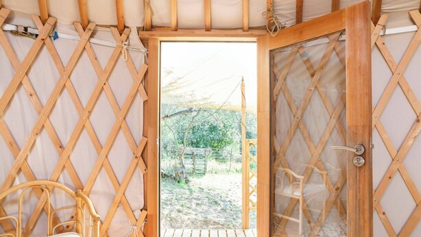 A wooden lattice room with a door leading outside, a wooden bench, and a small table. - A yurt among olive trees and the sea (Rapallo)