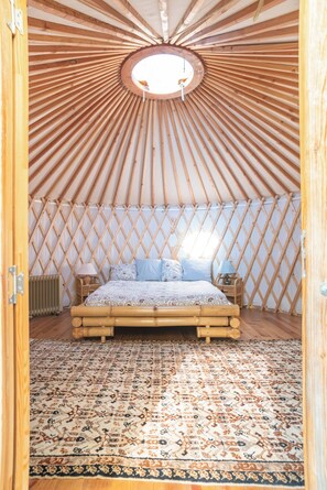Un interno circolare in legno con un letto, un tappeto decorato e un muro a griglia.