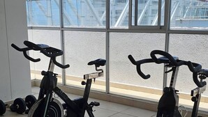 Två motionscyklar i ett gym med stora fönster och utsikt över en utomhuskonstruktion.