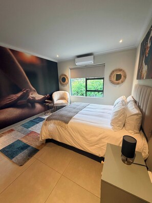 Un dormitorio con cama, una silla, un ventanal con vistas y aire acondicionado instalado en la pared.