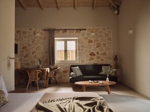 Ein gemütlicher Raum mit einem Bett, einem Holztisch, einem dunkelgrünen Sofa, einem Korbstuhl, einem Esstisch und einem Fenster mit Vorhängen.