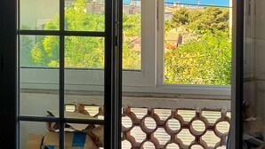 Ein Zimmer mit einem großen Fenster, einem Korbstuhl, einem kleinen Tisch und einem blauen Sessel.