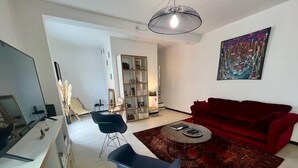 Ein Wohnzimmer mit einem roten Sofa, zwei blauen Sesseln, einem Couchtisch, einem Bücherregal und einem Gemälde an der Wand.
