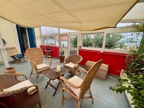A covered patio with wicker furniture, a table, and a view of the outside. - The original (Sète)