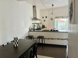 A compact kitchen with a dining area, a stove, a microwave, and a sink. - The original (Sète)