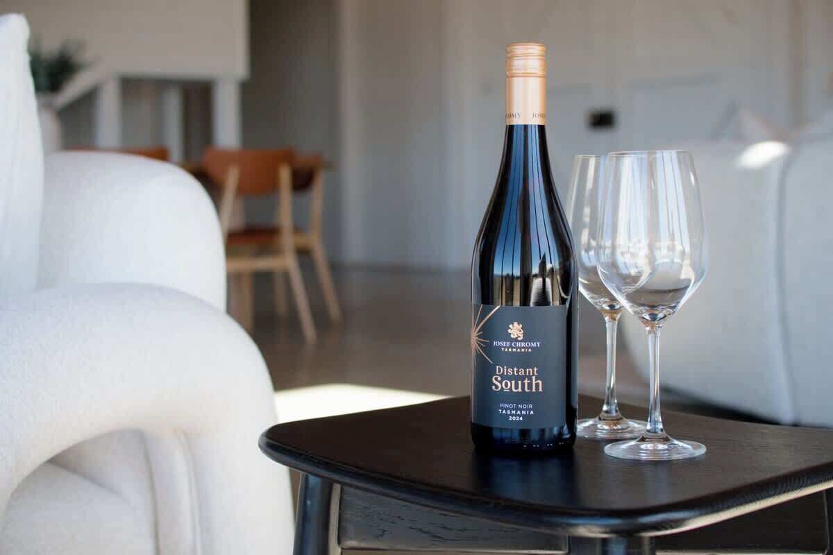 A bottle of wine and two glasses on a table in a modern room with a white couch and a wooden chair.