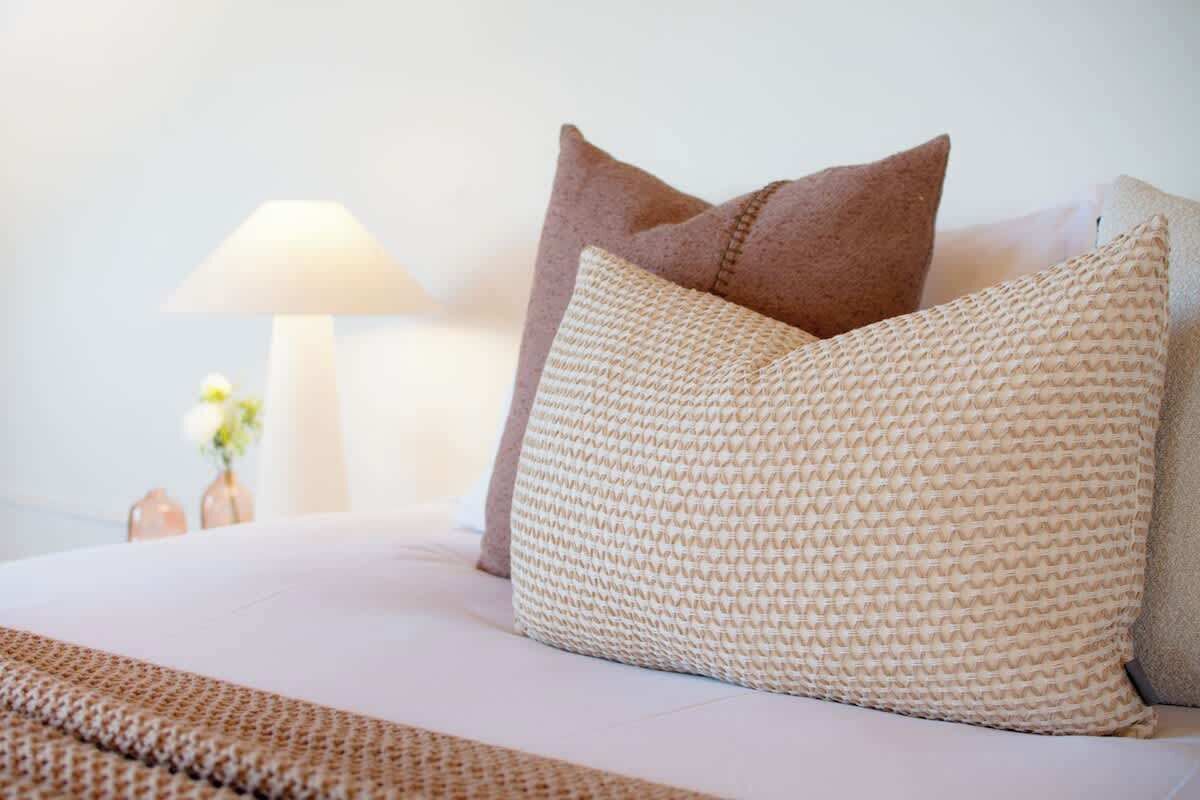 Ein Bett mit weißer Decke und zwei Kissen, eine Nachttischlampe und eine Vase mit Blumen.