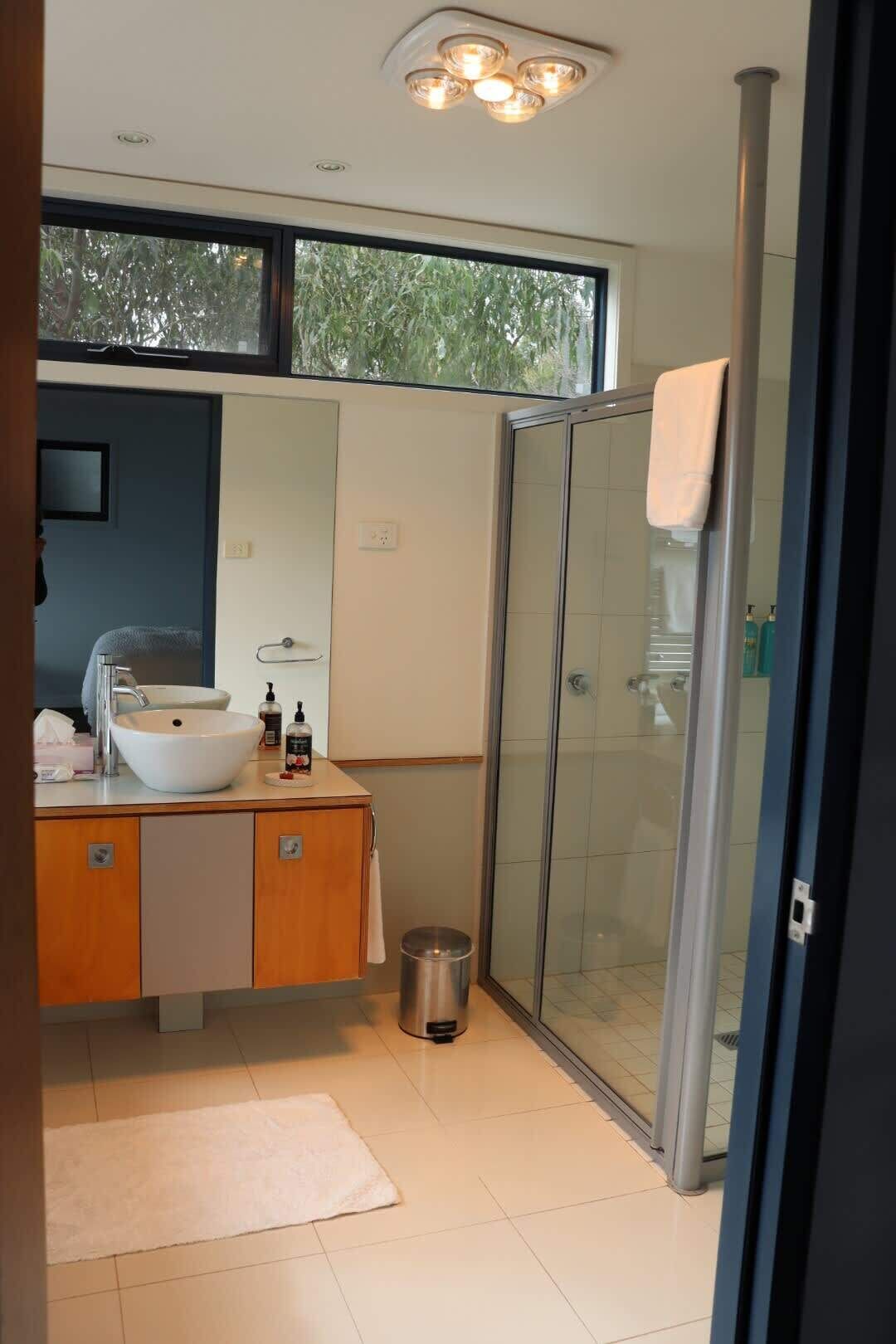 Ein modernes Badezimmer mit Duschkabine aus Glas, einem weißen Waschbecken und einem Holz-Waschtisch.