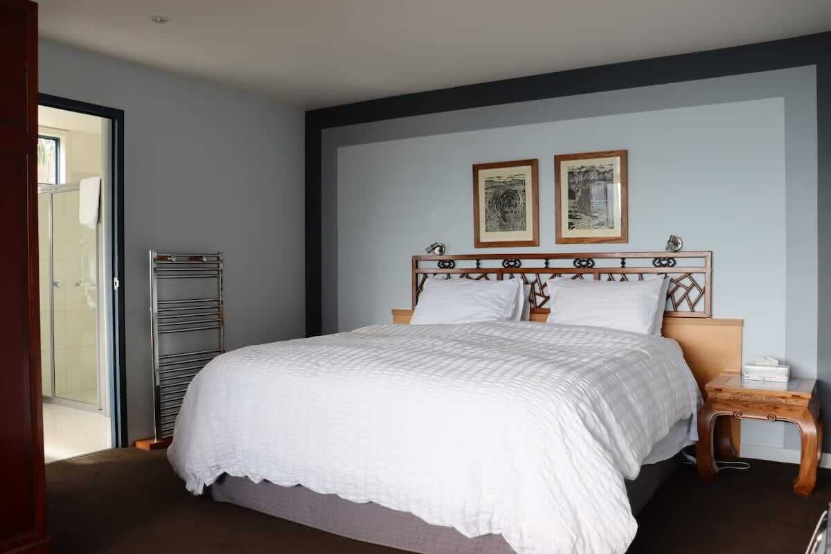 A bedroom with a bed, a nightstand, a wooden side table, and two framed pictures on the wall.