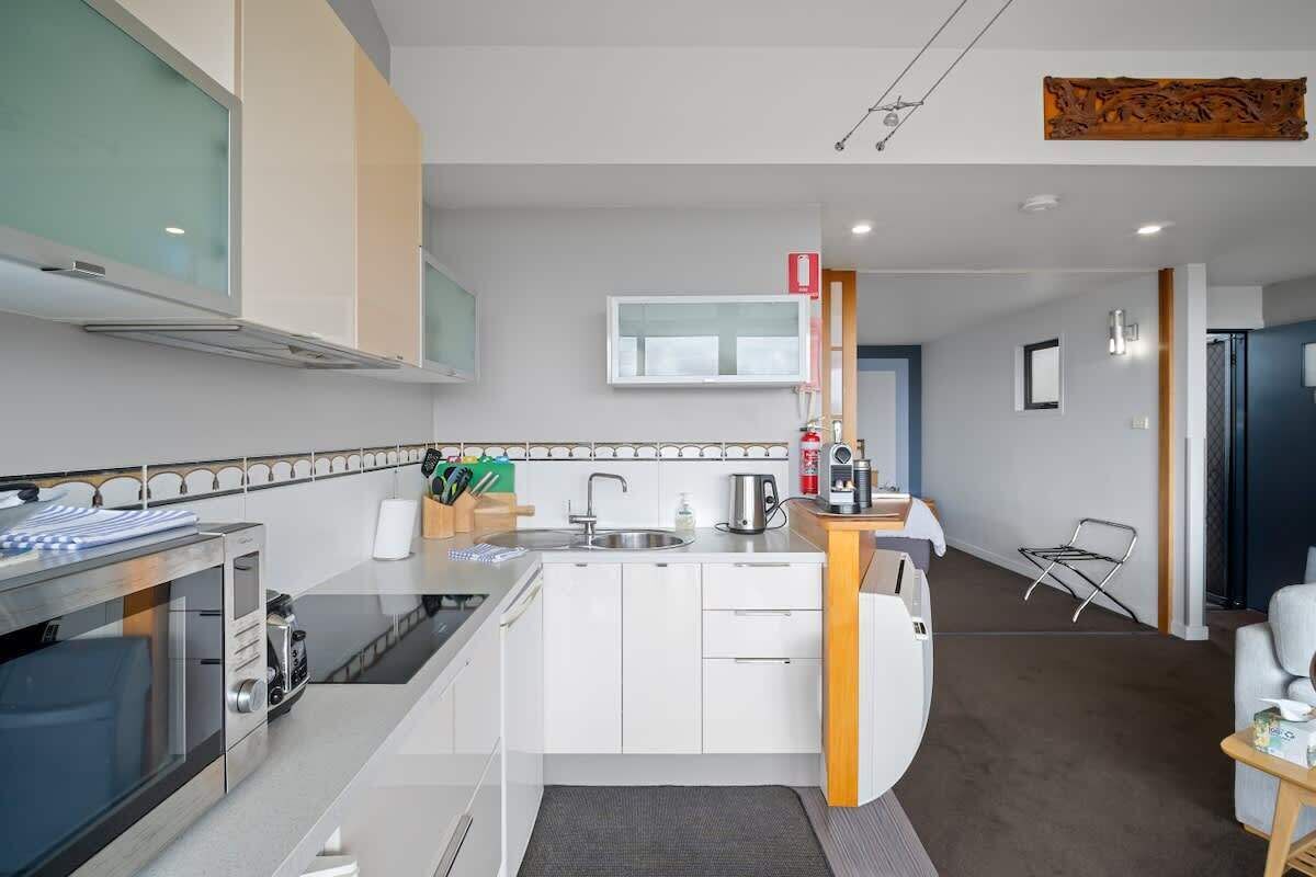 Une cuisine moderne avec des meubles blancs, un four encastré et un four à micro-ondes. On y trouve un petit îlot central avec un évier et une bouilloire.